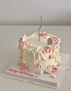 a white cake with pink flowers and a happy birthday sign on it's side