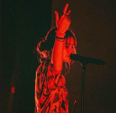 a woman standing in front of a microphone and raising her hand up to the sky