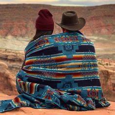 two people sitting on top of a cliff looking out at the desert and canyons