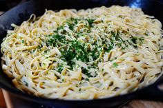 a pan filled with pasta and parsley on top of a wooden table