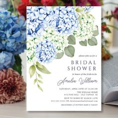 a wedding shower card with blue hydrangeas and greenery on the front, next to a bouquet of flowers