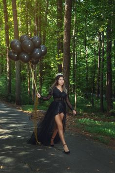 a woman in a long black dress is holding some balloons and posing for the camera