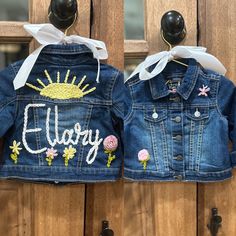 two children's denim jackets with embroidered words and flowers on them hanging from hooks