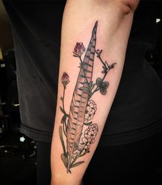 a woman's arm with a feather and flowers tattoo on the left upper arm