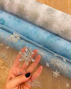 someone's hand next to three rolled up snowflakes