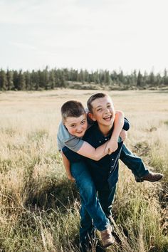 two young boys are hugging in the middle of a field with tall grass and trees behind them