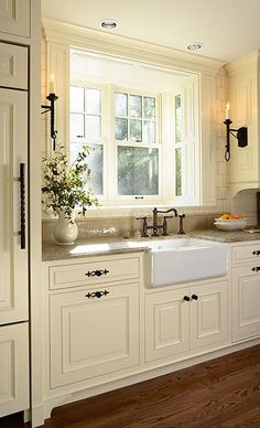 a white kitchen sink sitting under a window next to a vase with flowers in it