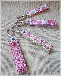 three keychains with flowers and hearts on them sitting on a fabric surface,