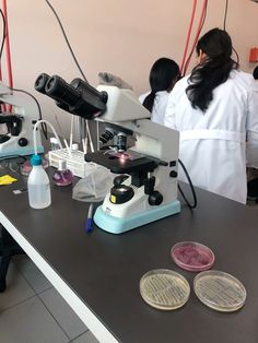 two people in lab coats looking through microscopes at some coins and other items on a table