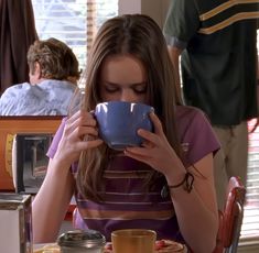 a woman sitting at a table drinking from a cup