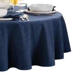 a blue table cloth with white plates and silverware on it, next to wine glasses