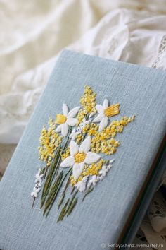 a blue book with yellow and white flowers on it sitting on a lace doily