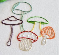 three different types of embroidered mushrooms on a white surface with green thread and scissors in the background