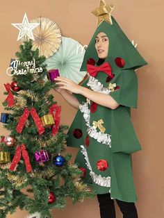 a woman dressed as a christmas tree holding a fan next to a decorated christmas tree