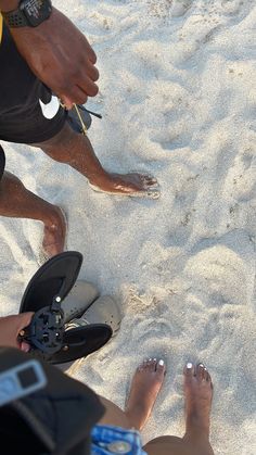 two people standing in the sand with their feet up and one person wearing flip flops