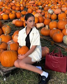 a woman is sitting on the ground surrounded by pumpkins