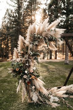 a wedding arch decorated with dried flowers and pamodia leaves in front of trees