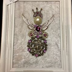 an ornate brooch in a white frame with purple stones and pearls on it's wings