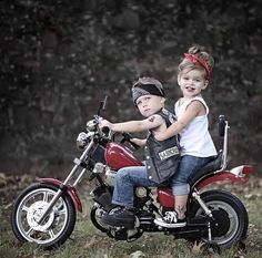 two children on a red motorcycle posing for a photo in front of some trees and grass