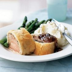 a white plate topped with meat and mashed potatoes next to green asparagus