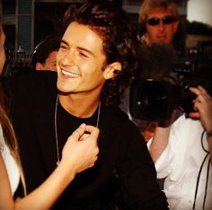 a young man smiling while being photographed by people