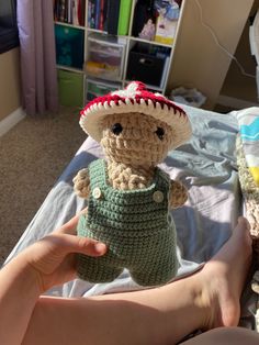 a crocheted teddy bear wearing a hat and overalls on top of a bed