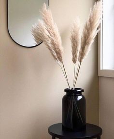 two white flowers in a black vase on a table next to a wall with a mirror