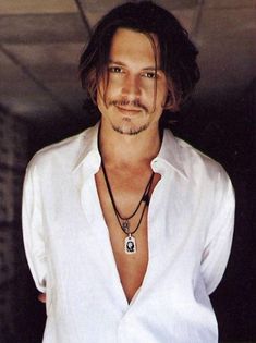 a man with long hair wearing a white shirt and holding a necklace on his neck