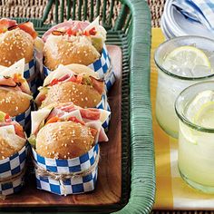 many sandwiches are wrapped in blue and white checkered paper on a tray next to drinks