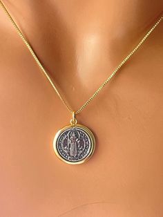 This is a 14 karat gold filled Saint Benedict pendant necklace for women. This Benedict coin actually swivels inside a 14 karat gold filled casing.  This two-tone charm comes with a shiny box chain. Pendant measures 17 mm in diameter. Model is wearing a 16 inch length box chain. Please choose your desired length. Available in 18 inch or 20 inch. If you choose a 20 inch chain you'll receive an 18 to 20 inch adjustable length. In a gift box ready to. St Benedict Necklace Gold, Tarnish Resistant 14k Gold Filled Medallion Jewelry, Spiritual Sterling Silver Coin Necklace In Yellow Gold, Gold Coin-shaped Jewelry With Charms, Spiritual Yellow Gold Sterling Silver Coin Necklace, 14k Gold Filled Coin Pendant Jewelry, 14k Gold Filled Jewelry With Coin Pendant, Dainty Nickel-free Medallion Jewelry, Yellow Gold Coin-shaped Charms Jewelry