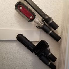 two black brushes sitting on top of a white wall next to a red and black brush