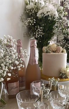 a table topped with lots of wine glasses next to bottles and vases filled with flowers