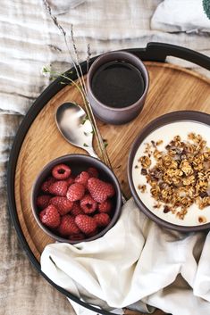 two bowls of cereal, yogurt and raspberries on a wooden tray