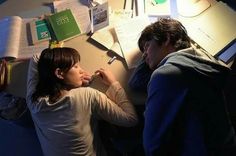 two people sitting at a desk with papers and pens