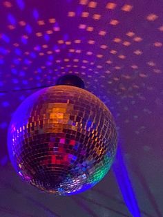 a disco ball hanging from the ceiling in front of purple and blue lights with stars on it