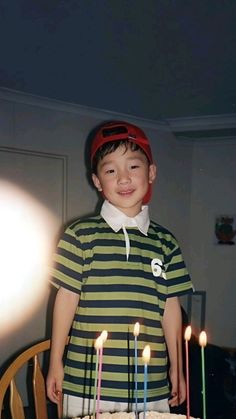 a young boy standing in front of a birthday cake with lit candles