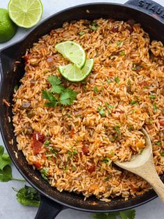 mexican rice in a skillet with limes and cilantro on the side