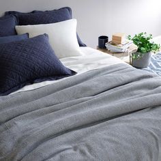 an unmade bed with blue and white comforters on it, next to a potted plant