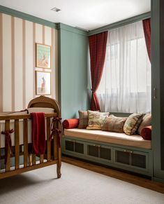 a baby's crib in front of a window with red drapes and striped curtains