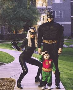 two adults and a child dressed up as batman and robin wayne in front of an apartment building