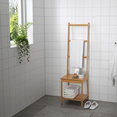 a white tiled bathroom with a wooden stand for towels and slippers on the floor