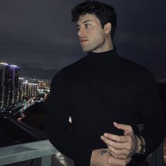 a man standing on top of a roof next to a tall building at night with city lights in the background