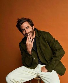 a man sitting on top of a stool with his hand to his face and smiling