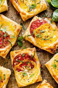 small square pizzas with tomatoes, cheese and herbs on a cutting board next to basil leaves