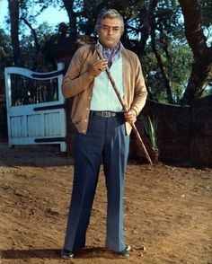 a man standing in the dirt holding a stick and wearing a jacket with a tie