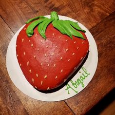 a strawberry shaped cake sitting on top of a white plate next to a wooden table