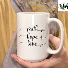 a woman holding a white coffee mug with the words faith and hope love on it