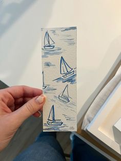 a person holding up a piece of paper with sailboats on it