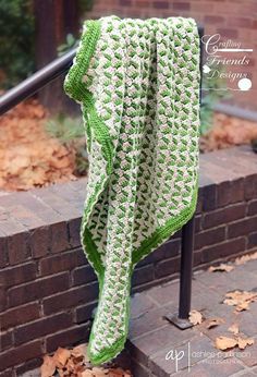 a green and white crocheted blanket hanging on a rail next to some leaves