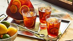 three glasses and two pitchers filled with oranges on a tray next to lemons